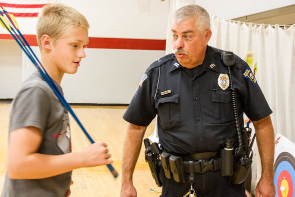 Police officer coaching a young boy on shooting a bow.