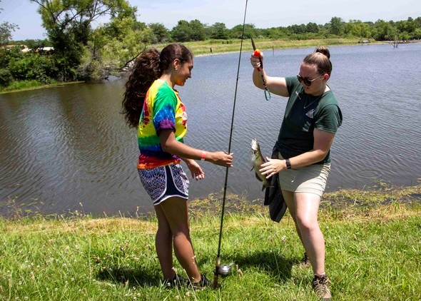 An MDC staff member teaches a teenager to fish.