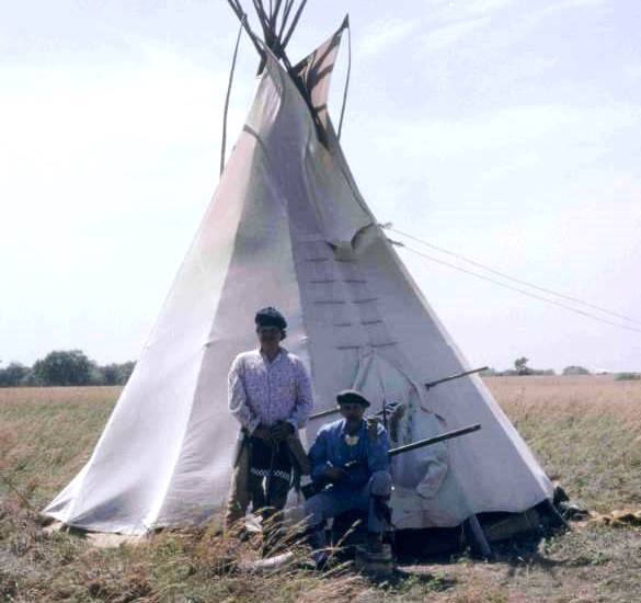 Two people dressed in frontier garb in front of a teepee