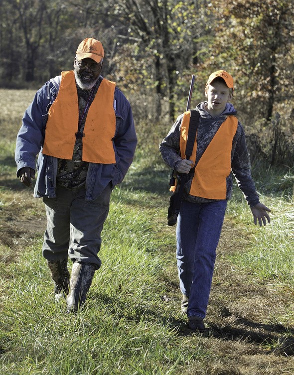 young hunter with mentor walking in field in camo