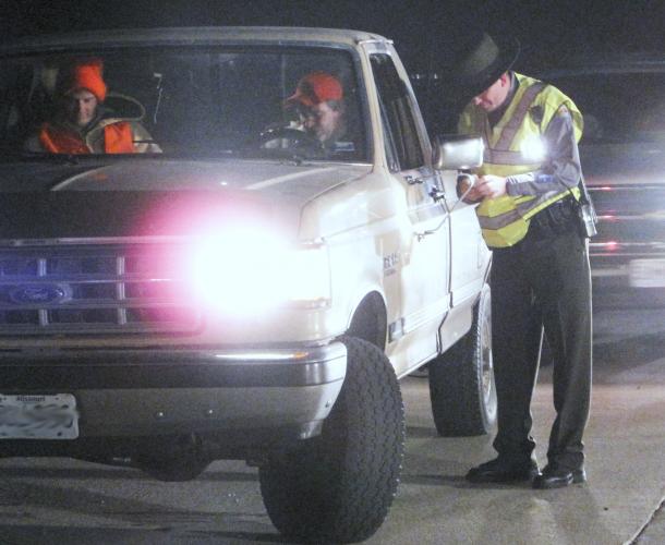A conservation agent at a checkpoint inspects permits for two hunters in a pickup truck 