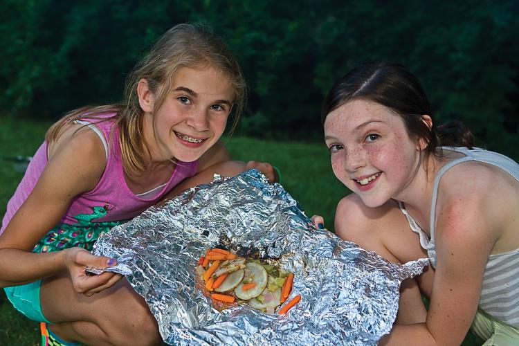 Two girls with a dish in tinfoil they cooked over a campfire.