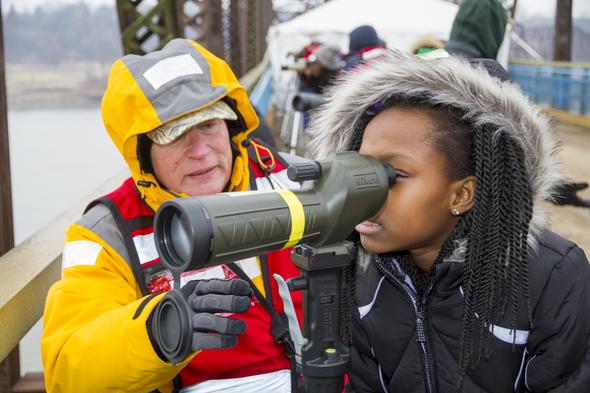 A lady helping a little girl look through a spotting scope for eagles.