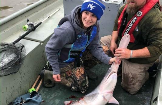 Two people hold snagged paddlefish on boat