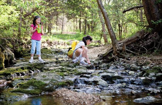 Girls drink from water bottle rather than creek while on hike.