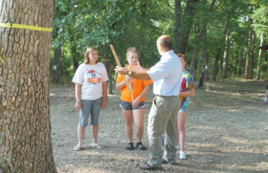 Two young women in shorts and t-shirts receive instruction from a forester.
