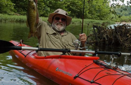 An angler in a bright red kayak holds aloft a fat, 2-pound smallmouth bass.