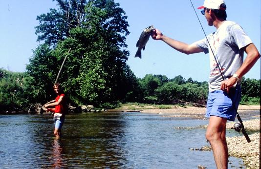 An angler holds up a smallmouth bass for his wade-fishing buddy to see.