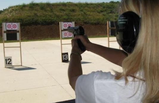 A woman uses a handgun to shoot at a target at an outdoor range.