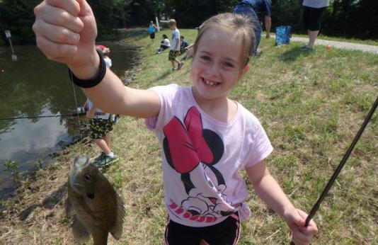 A girl in a Minnie Mouse t-shirt proudly holds up a small fish she caught