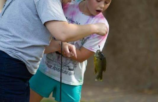 A volunteer helps a girl handle a small sunfish the girl just caught.