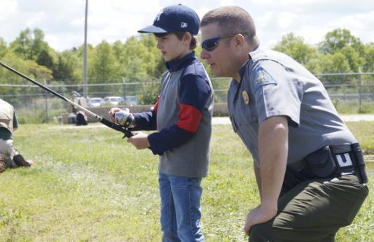 Conservation agent helping a little boy fish.