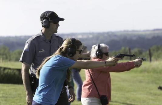 An MDC agent helps a woman learn to shoot a handgun.