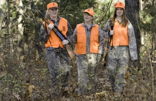 Three women walk through the woods while deer hunting