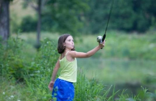 young girl casts a fishing rod and reel for trout fishing