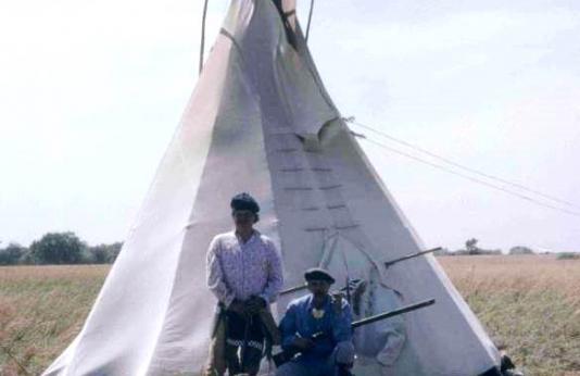Two people dressed in frontier garb in front of a teepee